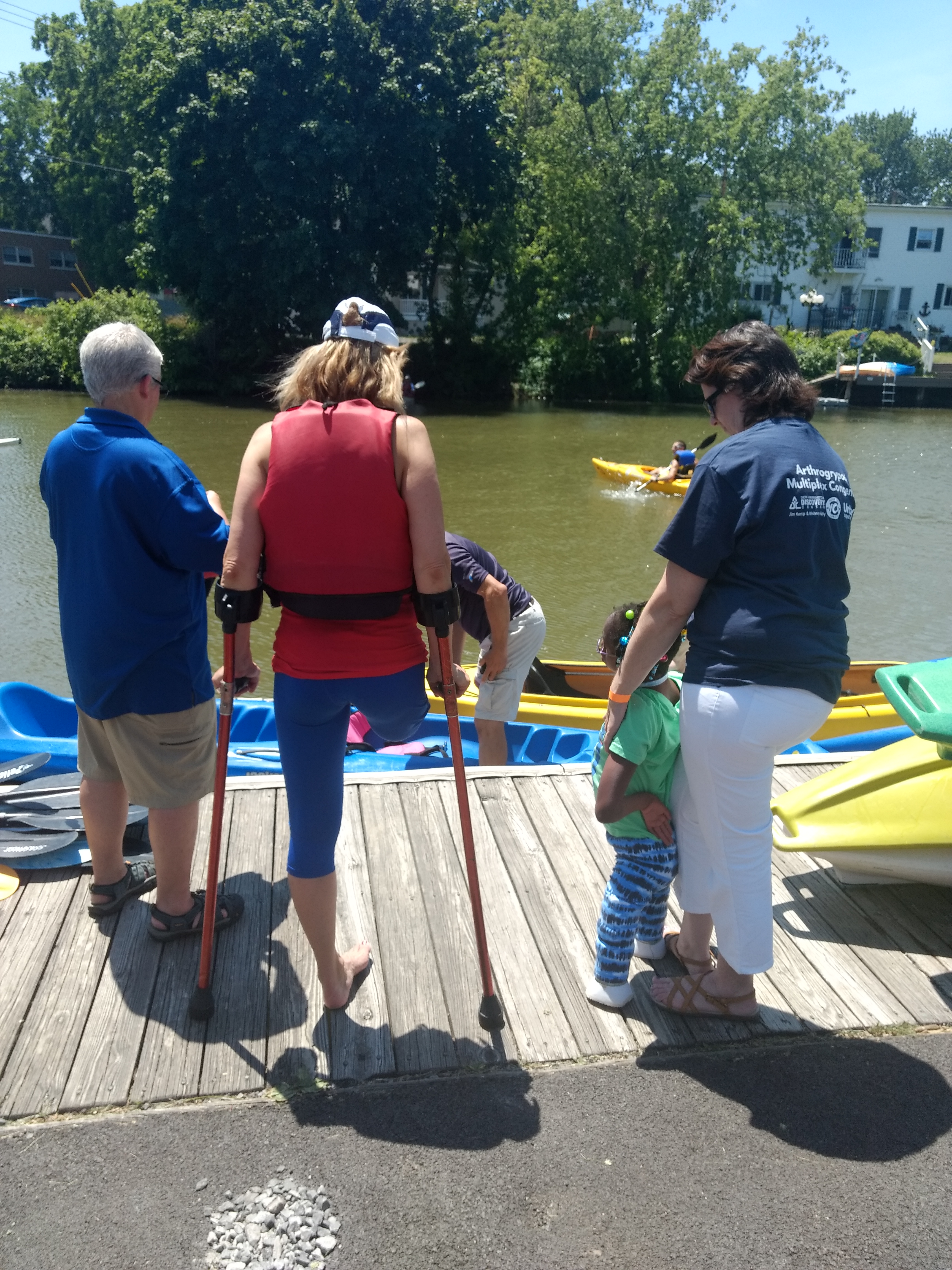 Three adults and one child, two with leg amputation, survey kayaks on a dock before going kayaking