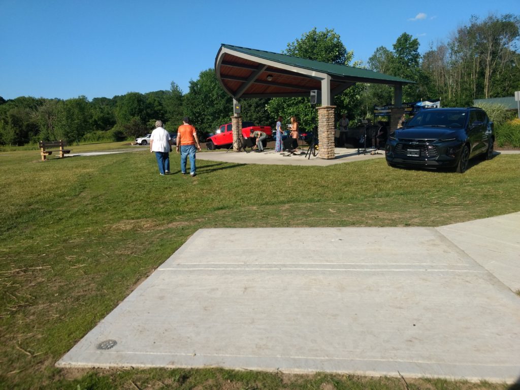 Concrete seating pad near the bandstand at Victor Municipal Park, people walking on the grass.