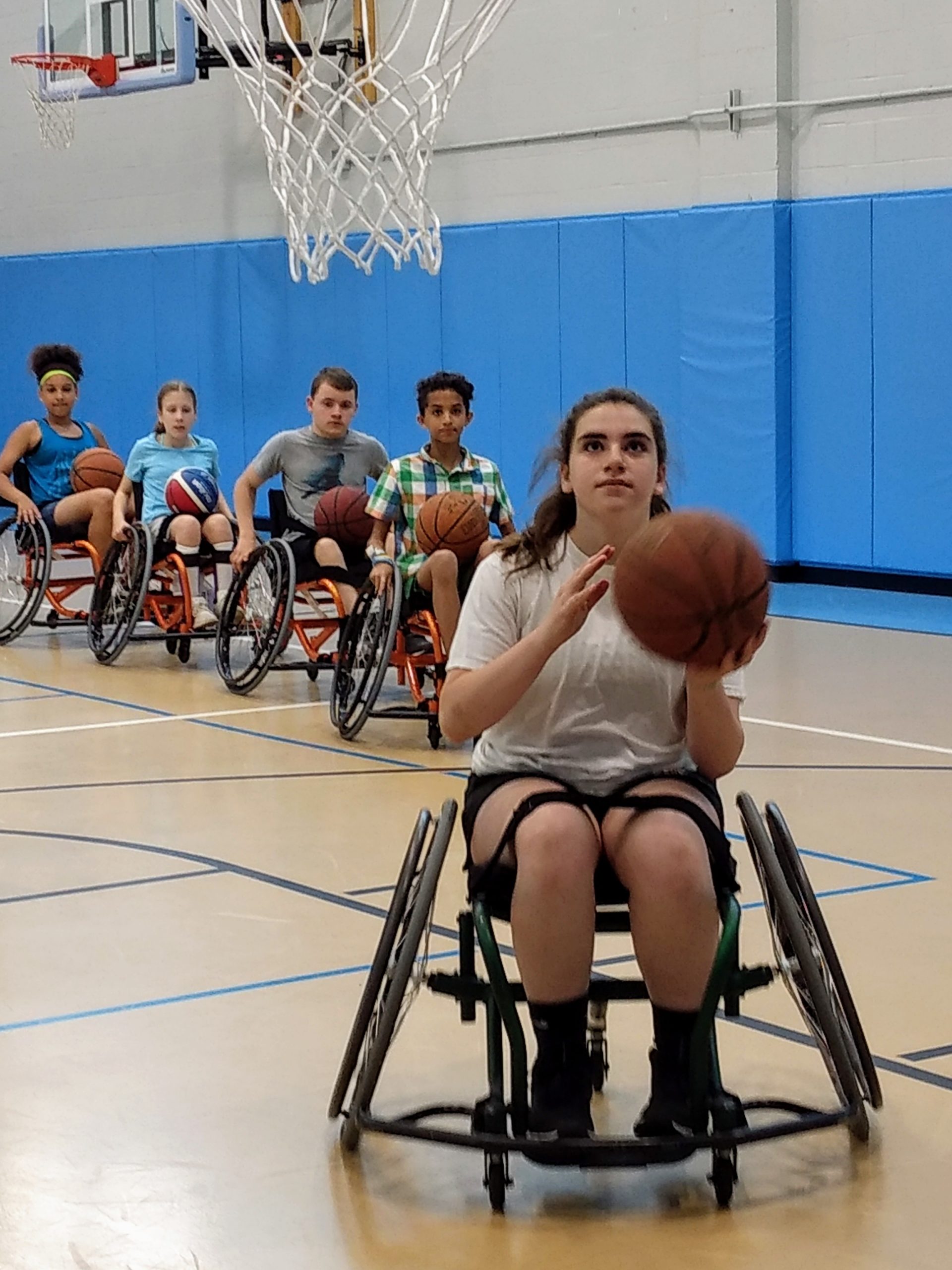Line of youth in sports wheelchairs get ready for shooting layups