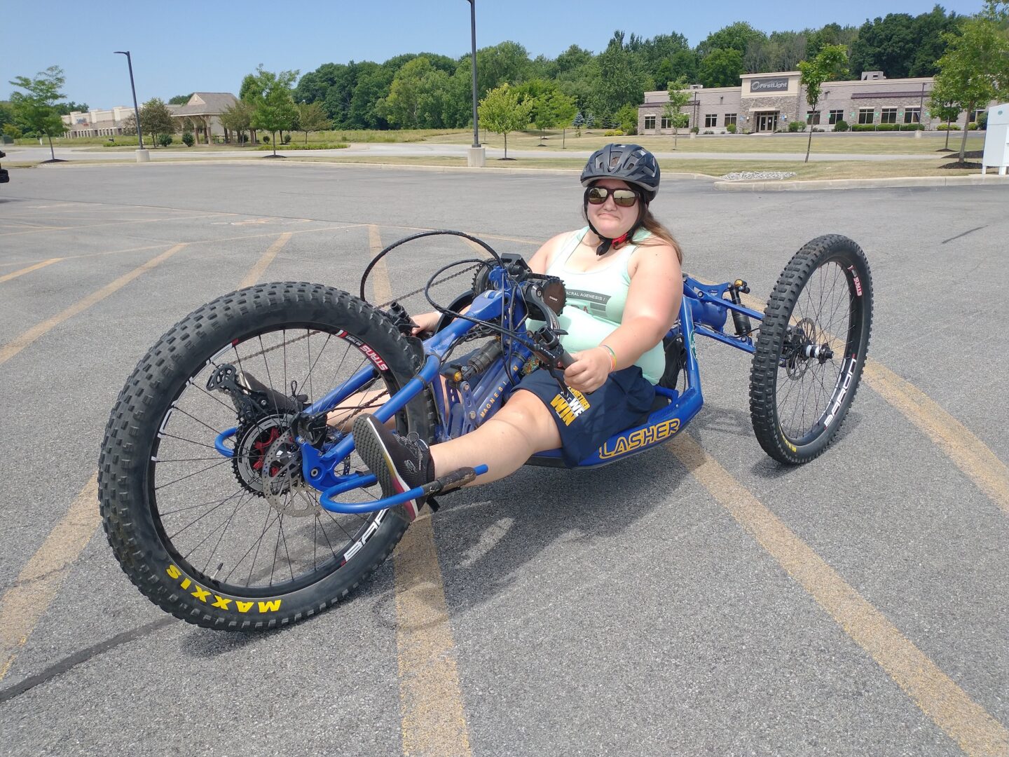 A woman sits on a hand-cranked adaptive mountain bike in a parking lot
