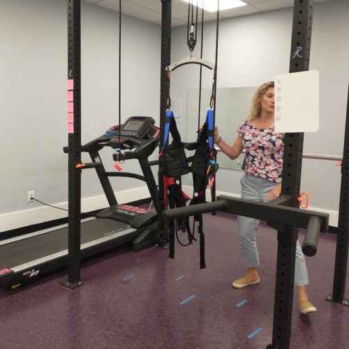 A woman stands behind a gait trainer and a treadmill