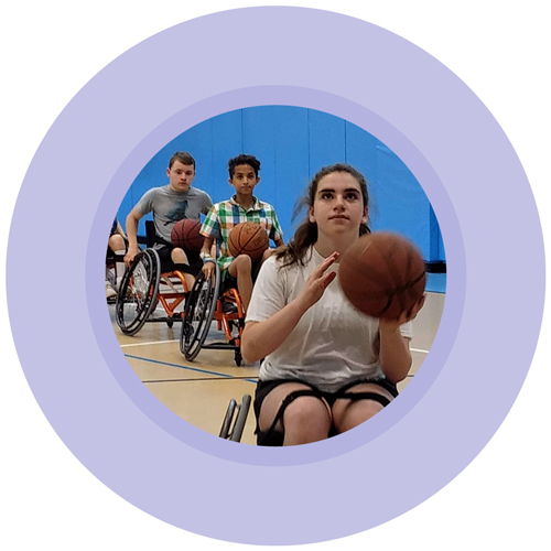 A closeup of three youth in a gym lined up for basketball layups; each in a sports chair and holding a basketball