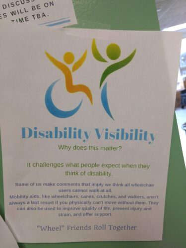 Picture of a flyer hanging on a wall; "Disability Visibility, Why does this matter? "Wheel" Friends Roll Together, artistic graphic of person in an wheelchair by a person standing.