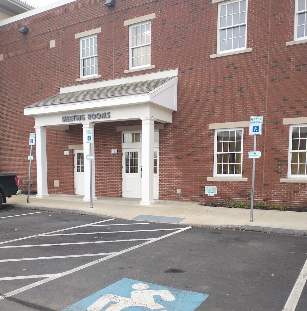An entrance to a building from the parking lot view of an accessible parking space with upright signpost and access aisle painted.