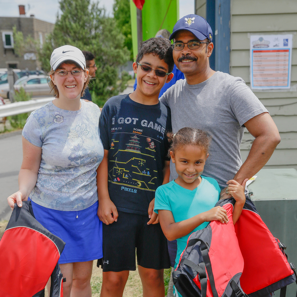 A family with two adults and two children stands together holding lifejackets and smiling.