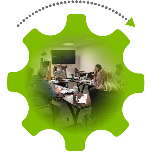 Green gear graphic with an arrow denoting movement; a photo inside the gear of people sitting around a table with papers in front of them