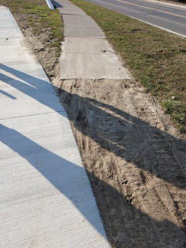 A cement pathway veers to the left while another sidewalk goes to the right; a small sandy/dirt area is a the intersection of the two paths