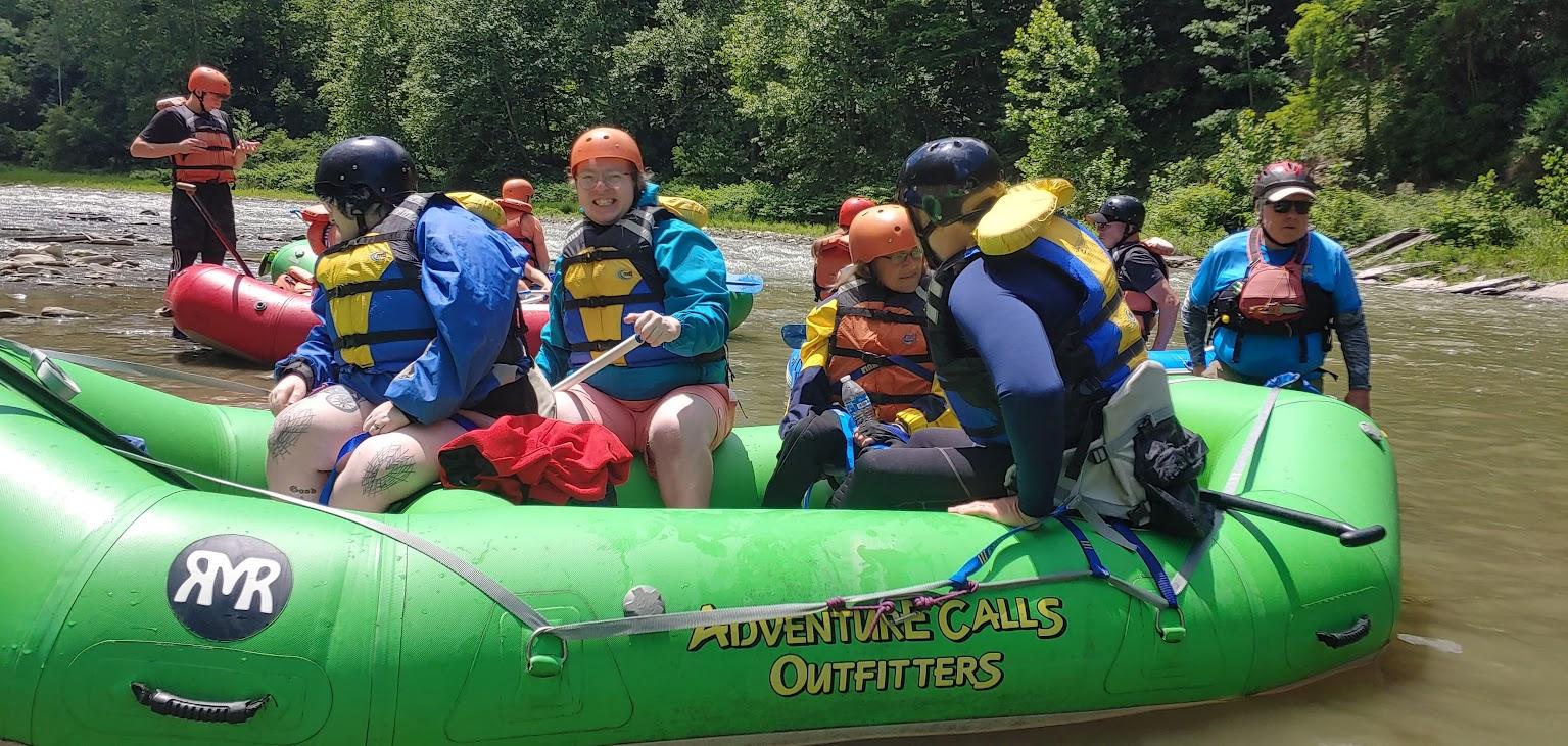 A group of people in a green whitewater raft on the Genesee River in Letchworth Gorge