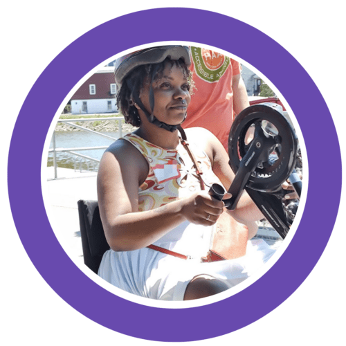 A purple circle frame around a woman of color riding a handcycle; she is dressed for the summer in a sleeveless tank and white skort. She has on a bike helmet.