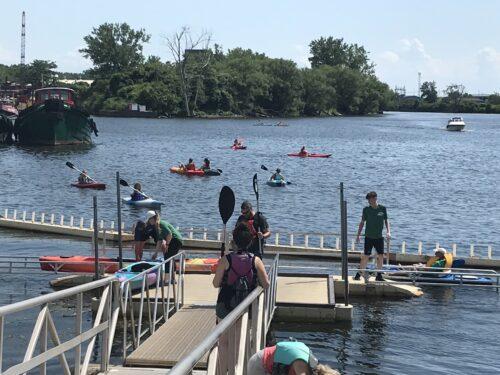 A view down the access ramp towards a kayak launch. People are in various places along the way, heading towards launching their kayaks.