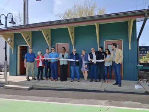 A group of people lined up behind a ribbon of toilet paper for a grand opening event for a changing station restroom in Fairport NY
