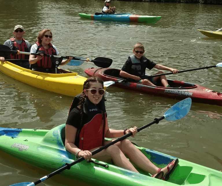 four family members are kayaking together with two in a tandem that has adaptive paddle stand in the front