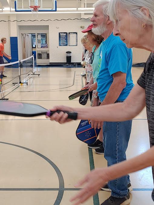 A closeup of a line of people in a gym with pickleball racquets hitting volleys or waiting for the ball to come to them