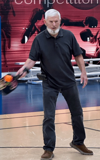 A man in black shirt and pants has a wide stance as he sets up to return a pickleball volley