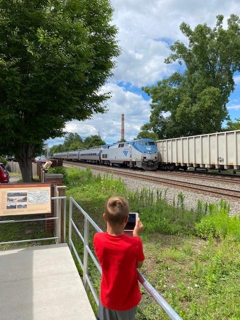 A youth records two trains passing on nearby tracks from a sheltered viewing platform