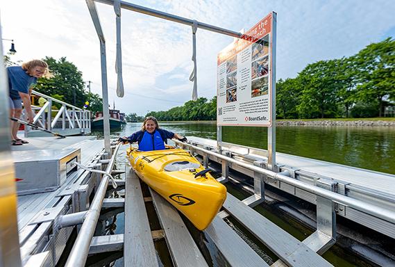 A woman smiles from a yellow kayak in the launching pad of a BoardSafe adaptive kayak launch