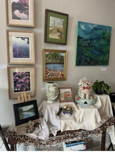 Various artworks and types of mediums are displayed on an art gallery wall and on a table below.