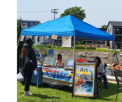 A blue tent along the shores of the Erie Canal showcases the art programs of Stony Point Art Studio with brightly painted signs and a table filled with art supplies