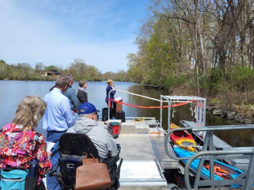 People stand on a dock by an adaptive kayak launch for a ribbon cutting ceremony