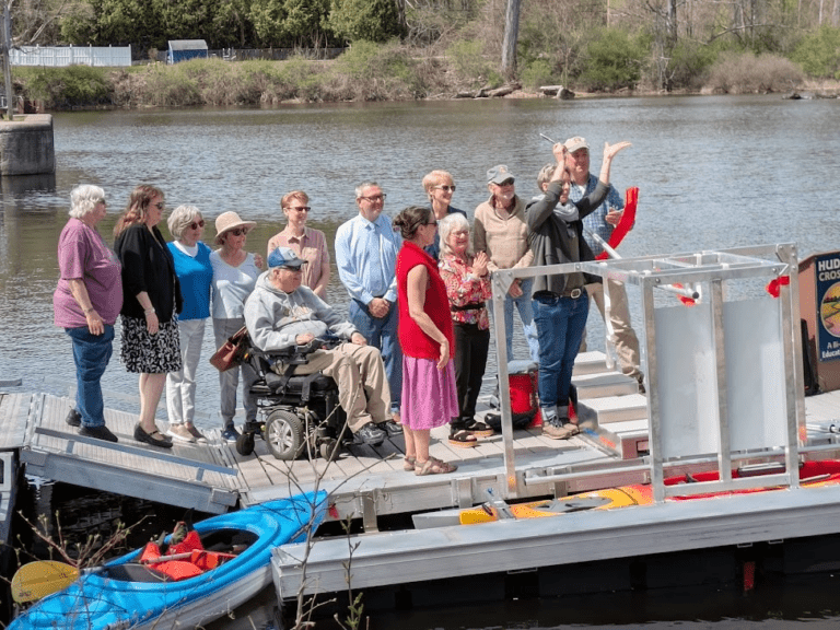 A group of people cheer as a ribbon is cut across a BoardSafe Kayak launch in Hudson Crossing Park.