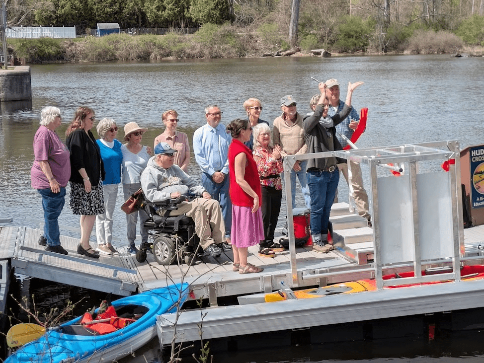 A group of people cheer as a ribbon is cut across a BoardSafe Kayak launch in Hudson Crossing Park.
