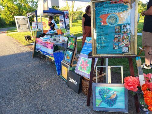 An outdoor table set up with many paintings and artistic displays highlighting art workshops with Stony Point Art Studio