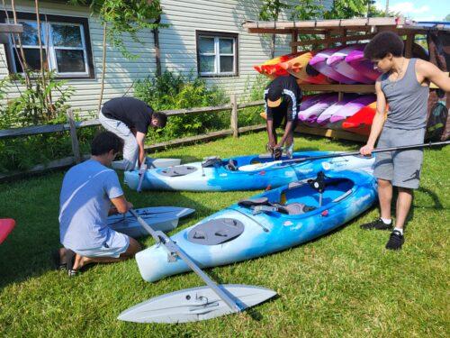 Three staff on the grass at Elevator Alley Kayak prepare kayaks with adaptive equipment pieces prior to an excursion.