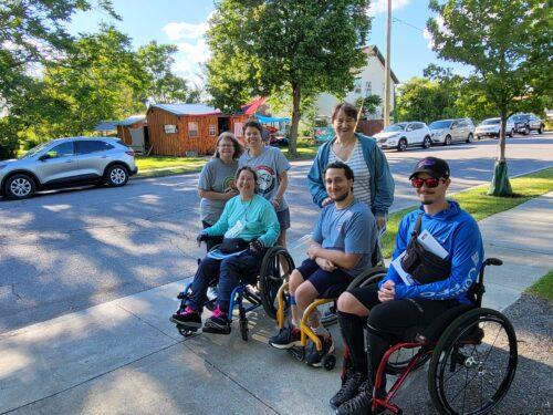 A group of six people pose for a photo after kayaking, including three people standing and three people in wheelchairs
