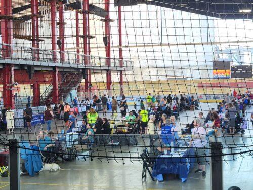 A wide view of one of two large arenas filled with rows of vendor tables and festival-goers.