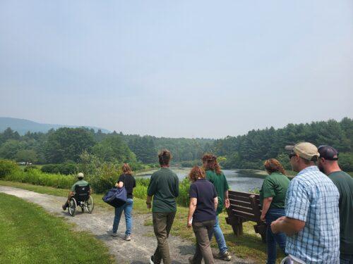 A workshop participant using a manual wheelchair on an access path leading to a fishing dock and kayak launch, assessing the route firsthand.
